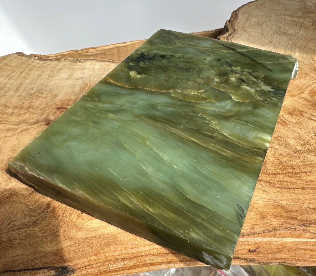 Flat green jade slab resting on a wooden surface, showing natural veins and rough edges
