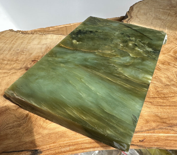 Flat green jade slab resting on a wooden surface, showing natural veins and rough edges