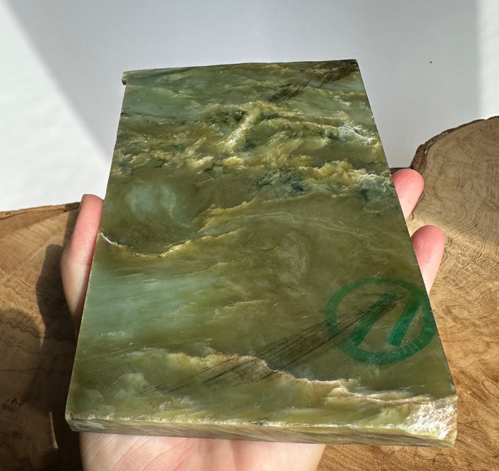 Rough green jade slab held in a hand showing layered colors and natural patterns