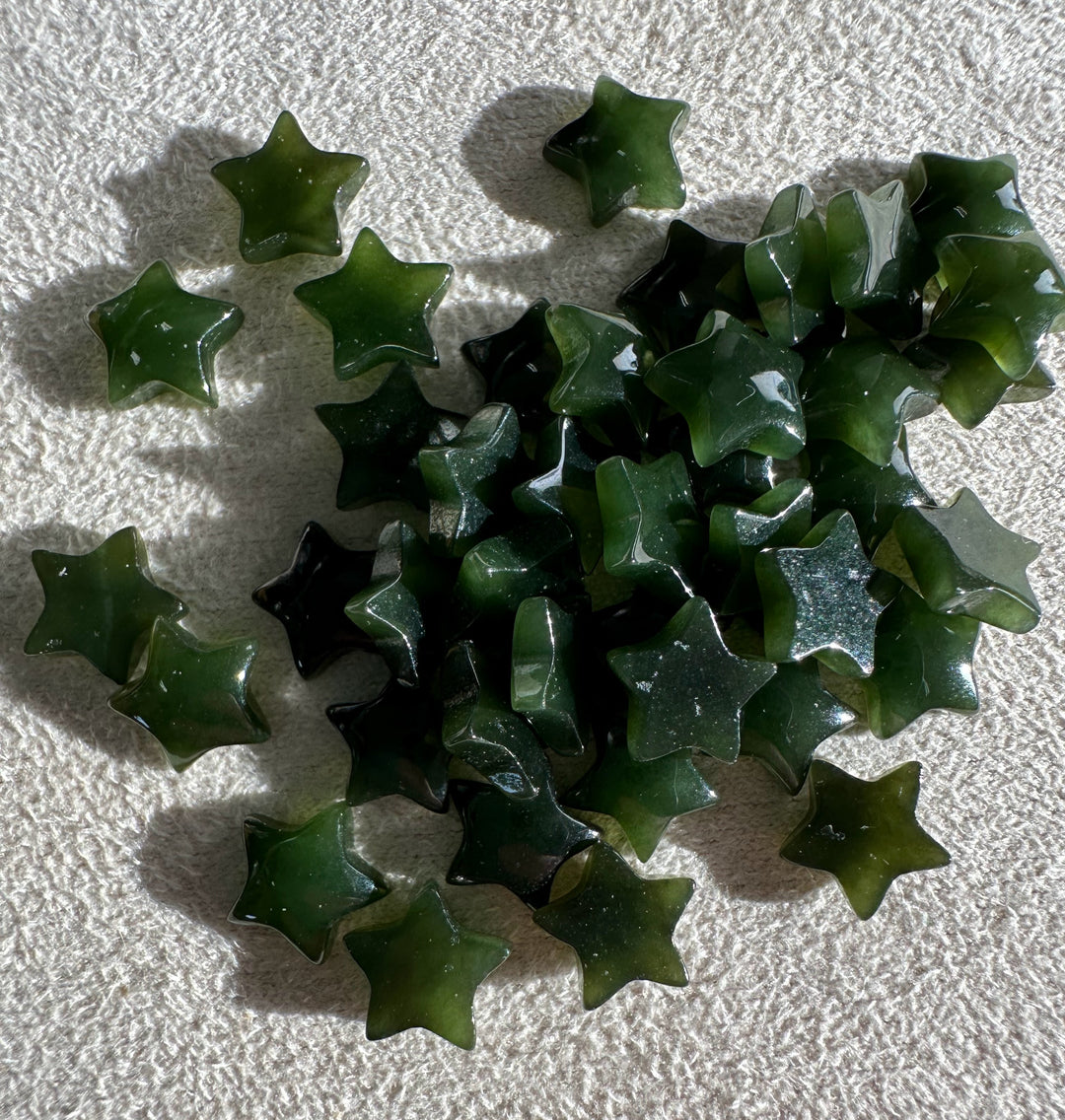Dark green jade star cabochons scattered on a light textured fabric background