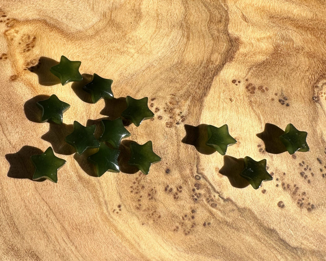 Dark green jade star cabochons scattered on a warm wood surface with grain patterns