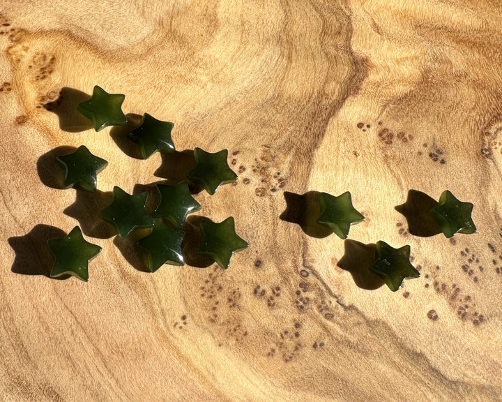 Dark green jade star cabochons scattered on a warm wood surface with grain patterns