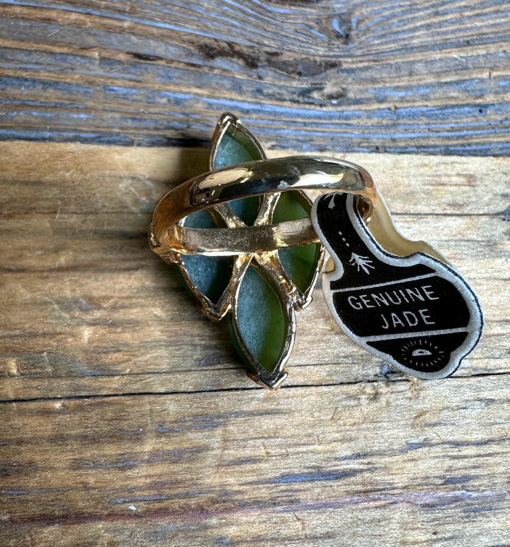 Gold ring with green jade in a leaf setting and Genuine Jade tag on a rustic wooden surface