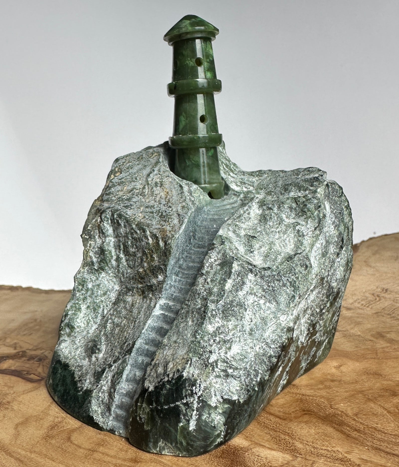 Green jade lighthouse sculpture perched on a rough rock base