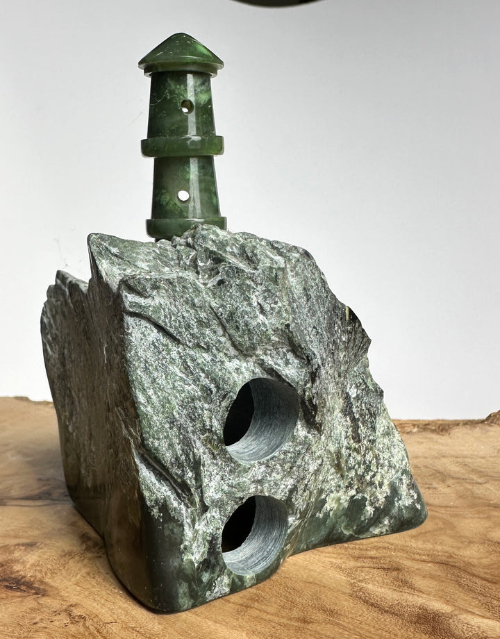 Hand holds a green jade lighthouse with circular holes in the column on a rugged rock base