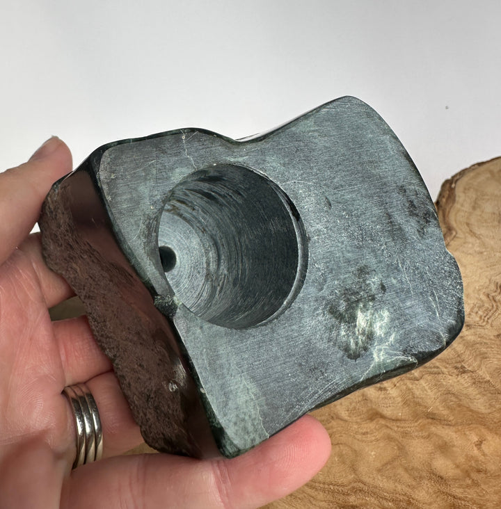Close up of a green jade lighthouse carving on a textured rock with a circular hollow in the base