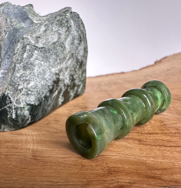 Partial view of a green jade lighthouse sculpture beside a rough rock on a wooden surface