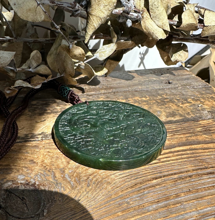 Dark green jade medallion resting on a rustic wooden surface with dried leaves in the background.