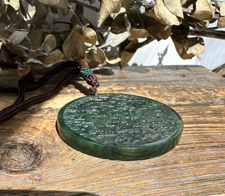 Circular dark green jade dragon and phoenix medallion with intricate carvings resting on a wooden surface.