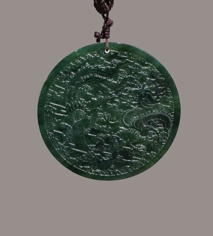 Circular dark green jade medallion with dragon and phoenix relief on a braided brown cord.