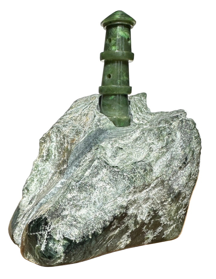 Green jade lighthouse sculpture perched on a rocky base against a white background