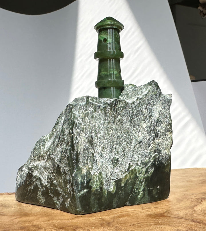 Tall green jade lighthouse sculpture atop a jagged rock with a light background