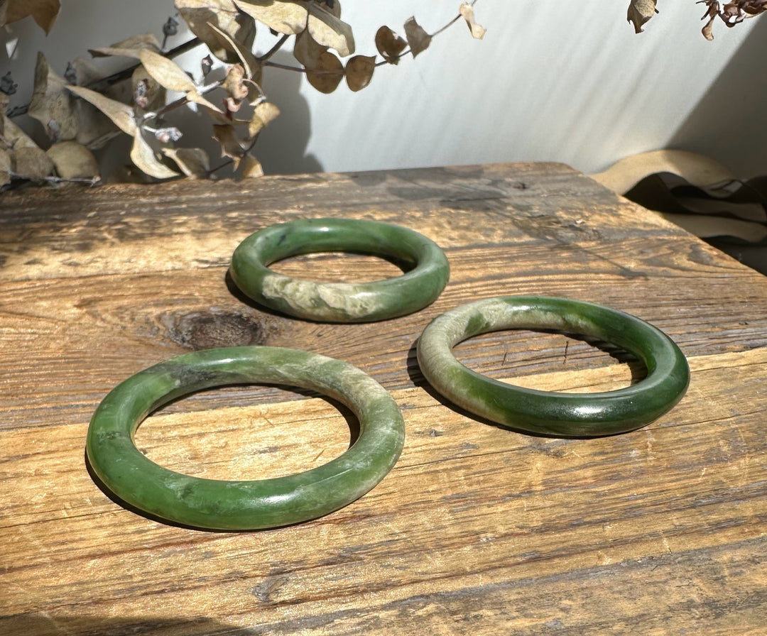 Three green jade bangles with varying tones on a weathered wooden table