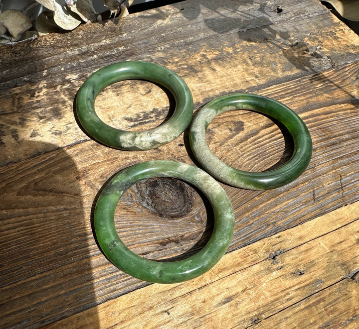 Three green jade bangles laid on a weathered wooden surface.