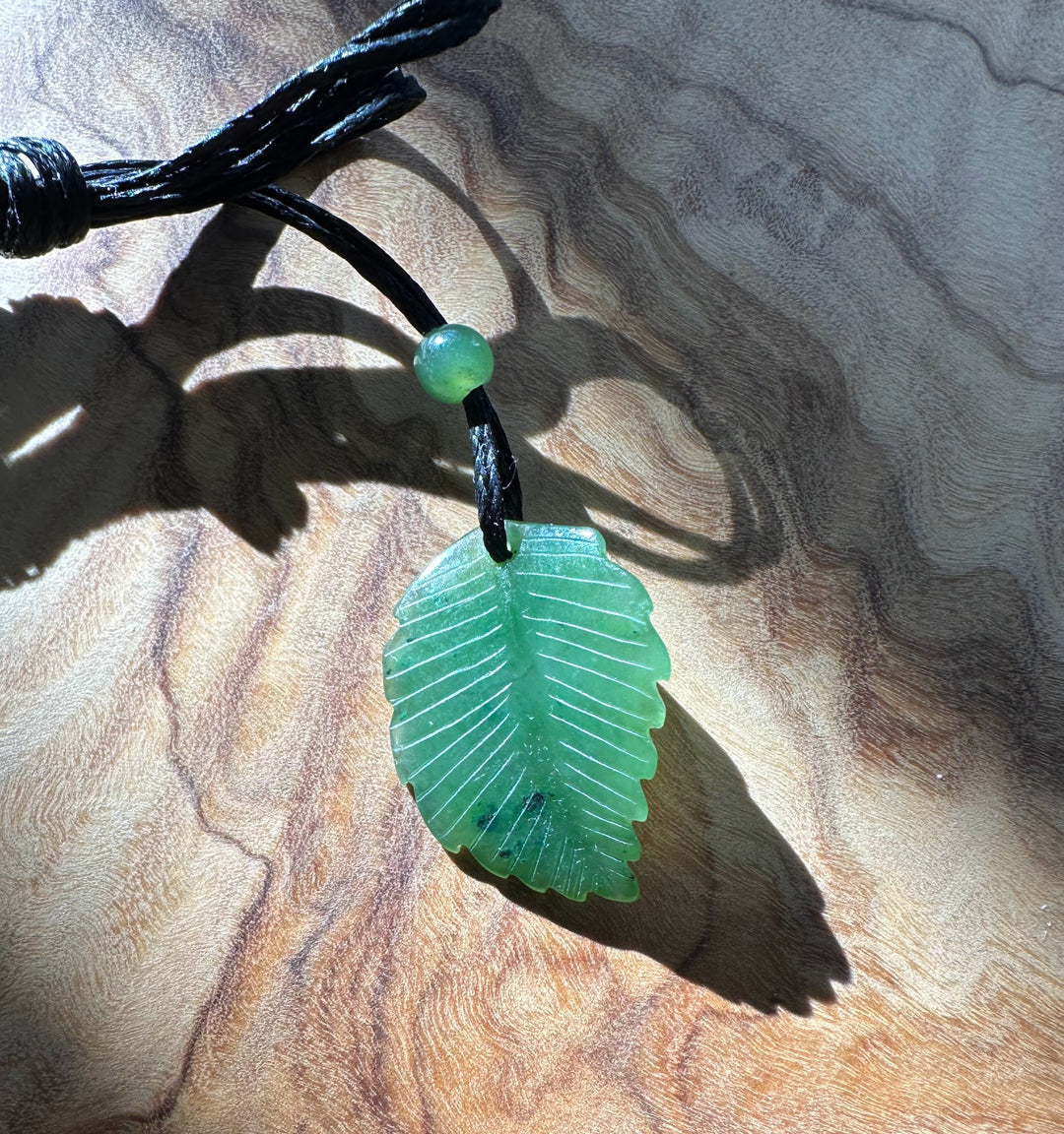 Front view of Canadian green jade leaf pendant on black cord necklace with bead above, showing leaf veins.