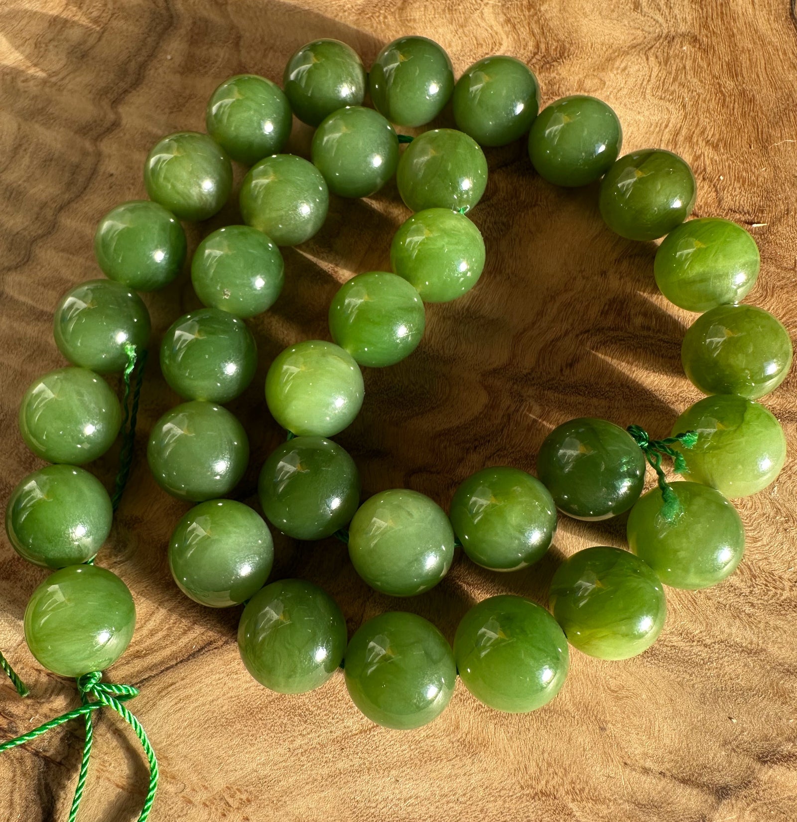Light green Canadian 12mm beads arranged in a circular strand on a wooden surface