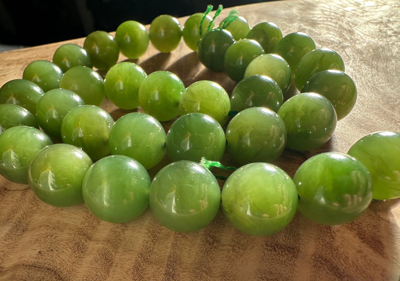 Close up of light green 12mm Canadian beads threaded on a green cord on wood