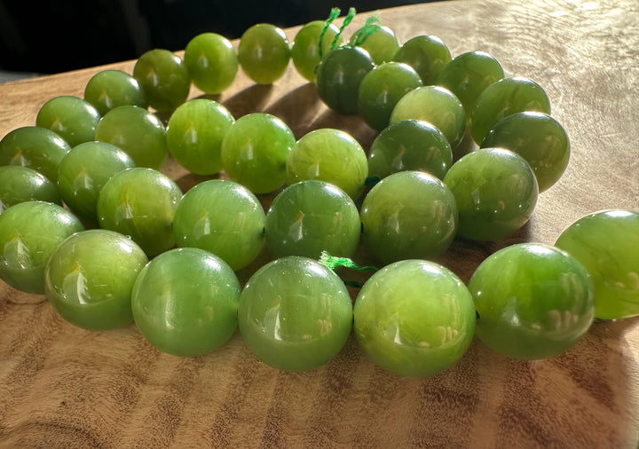 Close up of light green 12mm Canadian beads threaded on a green cord on wood