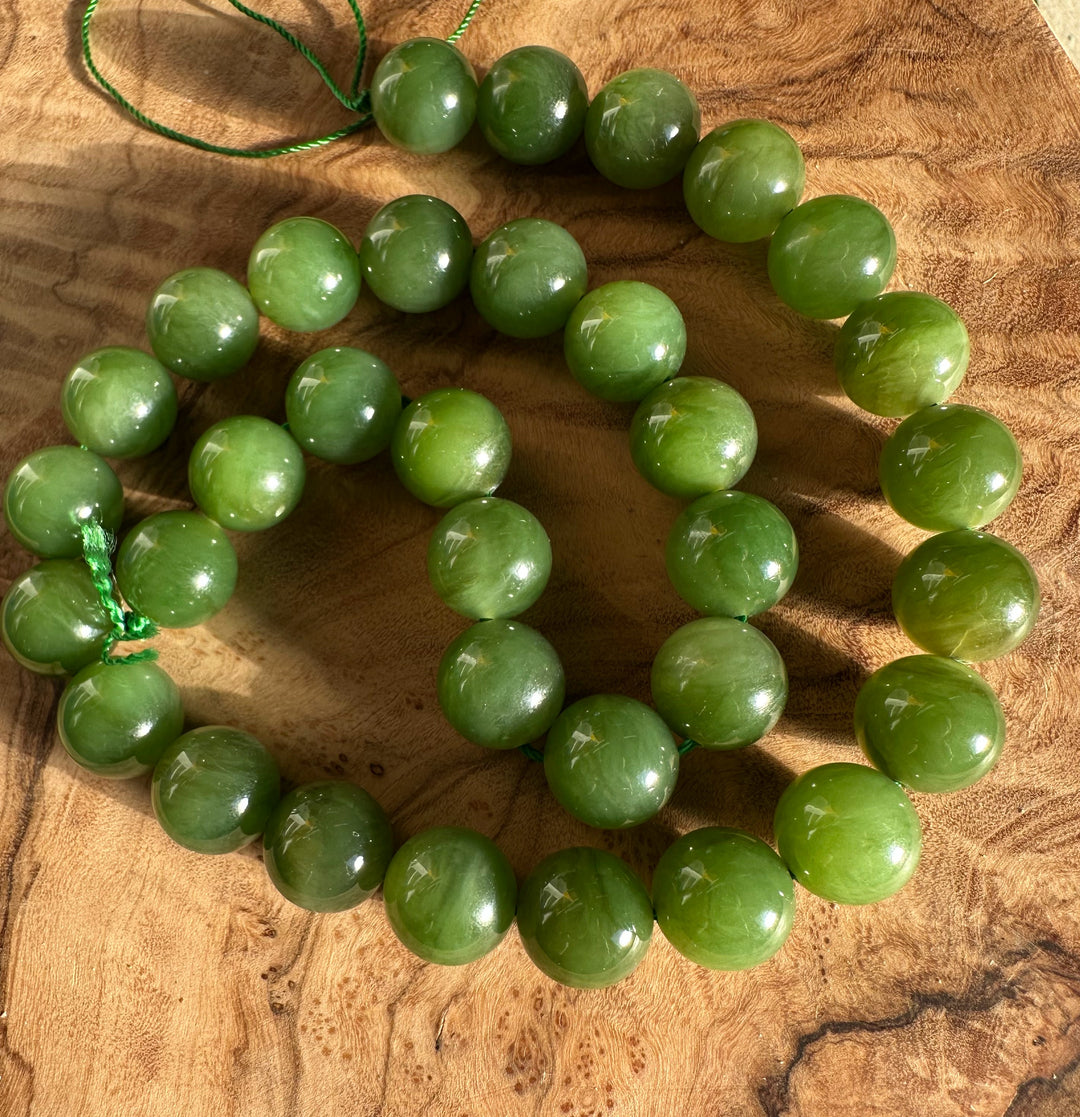 Unstrung light green 12mm Canadian beads on a green cord laid on a wooden surface