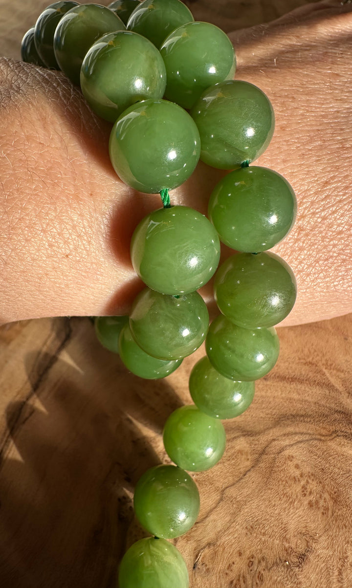 Glossy light green 12mm beads on a green cord worn as a bracelet on a wrist