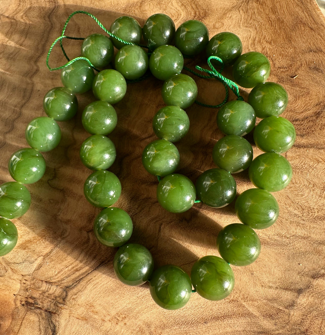 Light green 12mm beads strung on green cords arranged in loops on a wooden surface