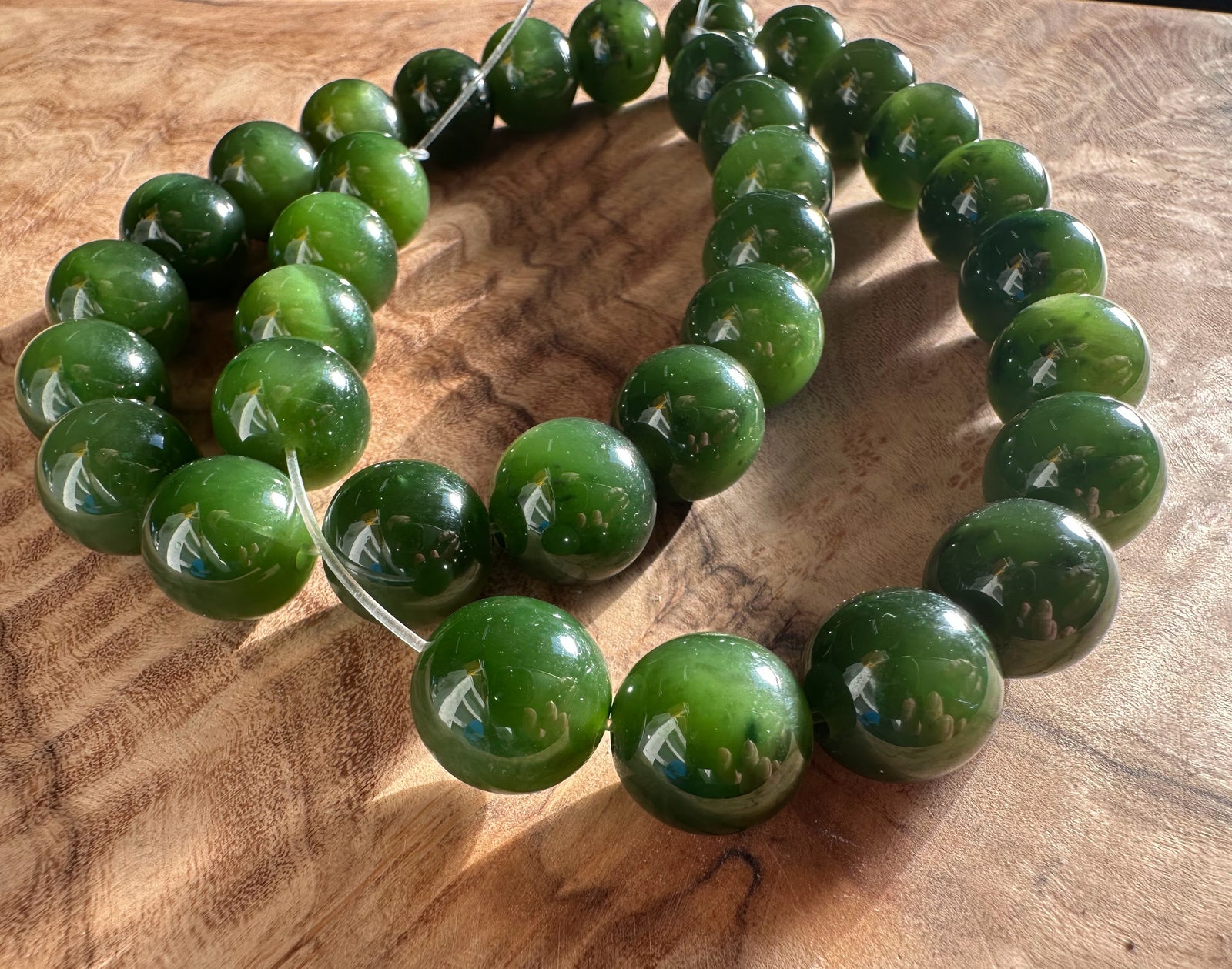 12mm Cassiar Jade beads on a string, glossy green, curved along a wood background