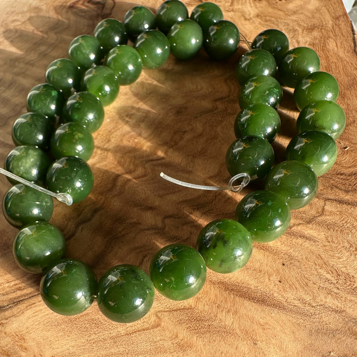 Unstrung 12mm Cassiar Jade beads arranged in a circle on a wooden surface