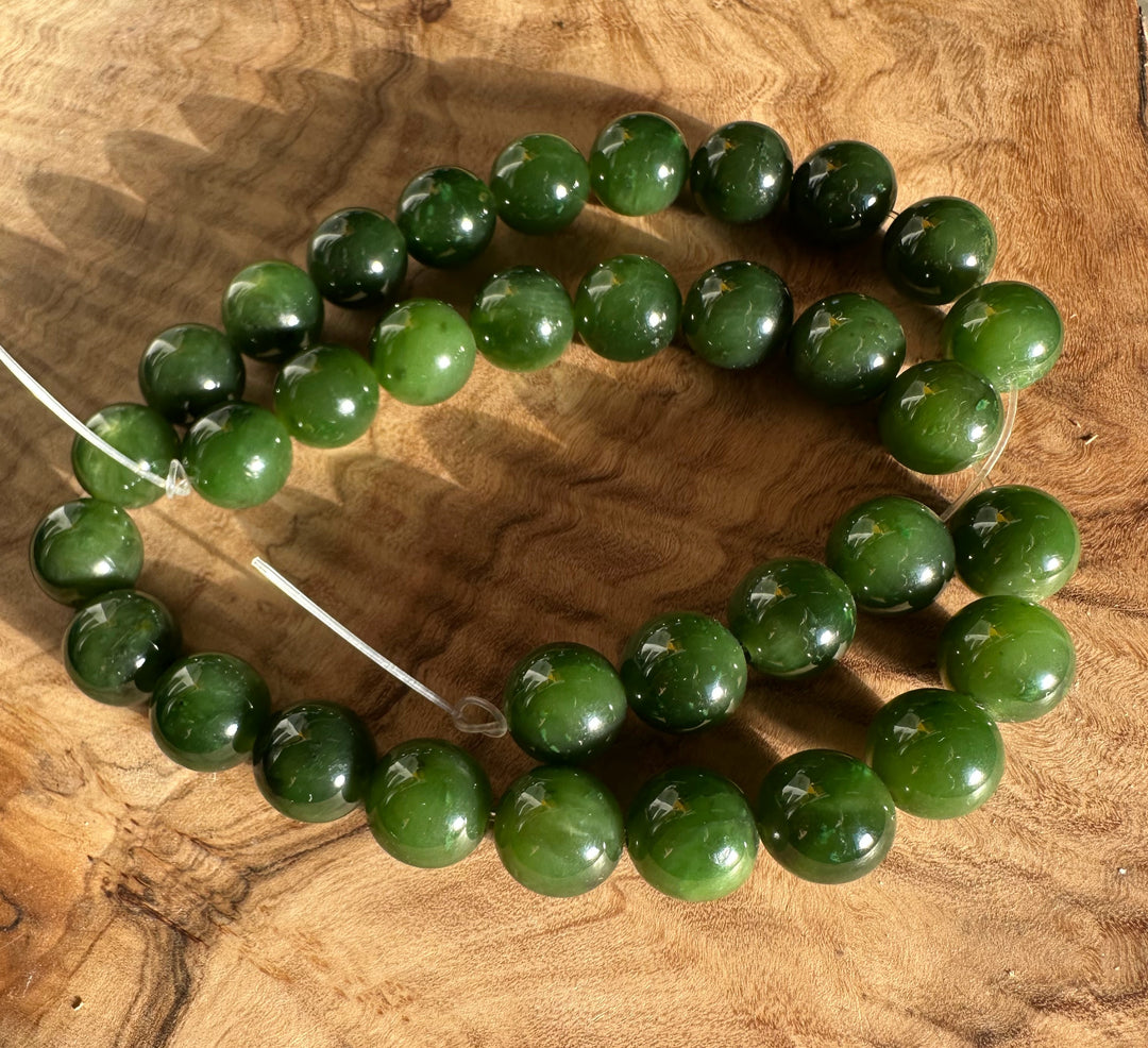 Unstrung 12mm Cassiar Jade beads arranged in a loose spiral on a wood surface.
