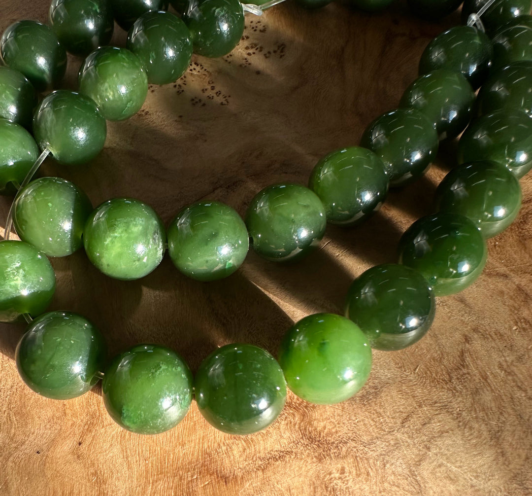 Close-up of glossy 12mm Cassiar Jade beads laid in a curved line on a wood surface.