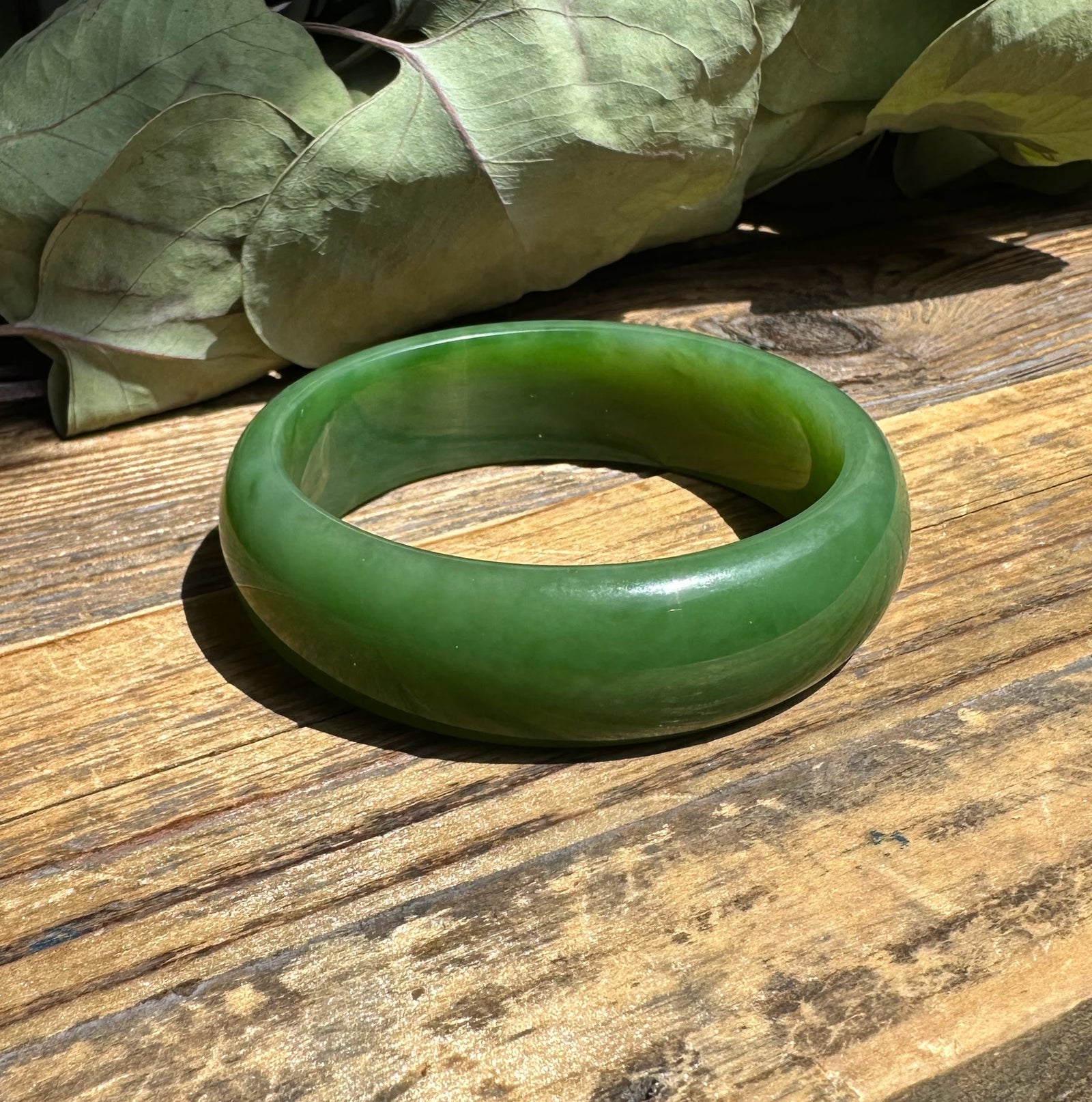 Green jade bangle resting on a weathered wooden table with dried leaves in the background.