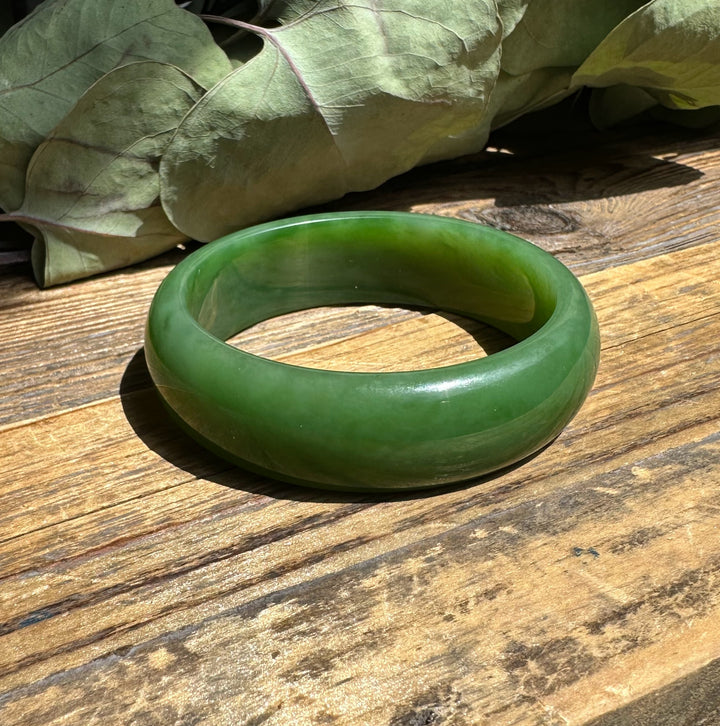 Green jade bangle resting on a weathered wooden table with dried leaves in the background.