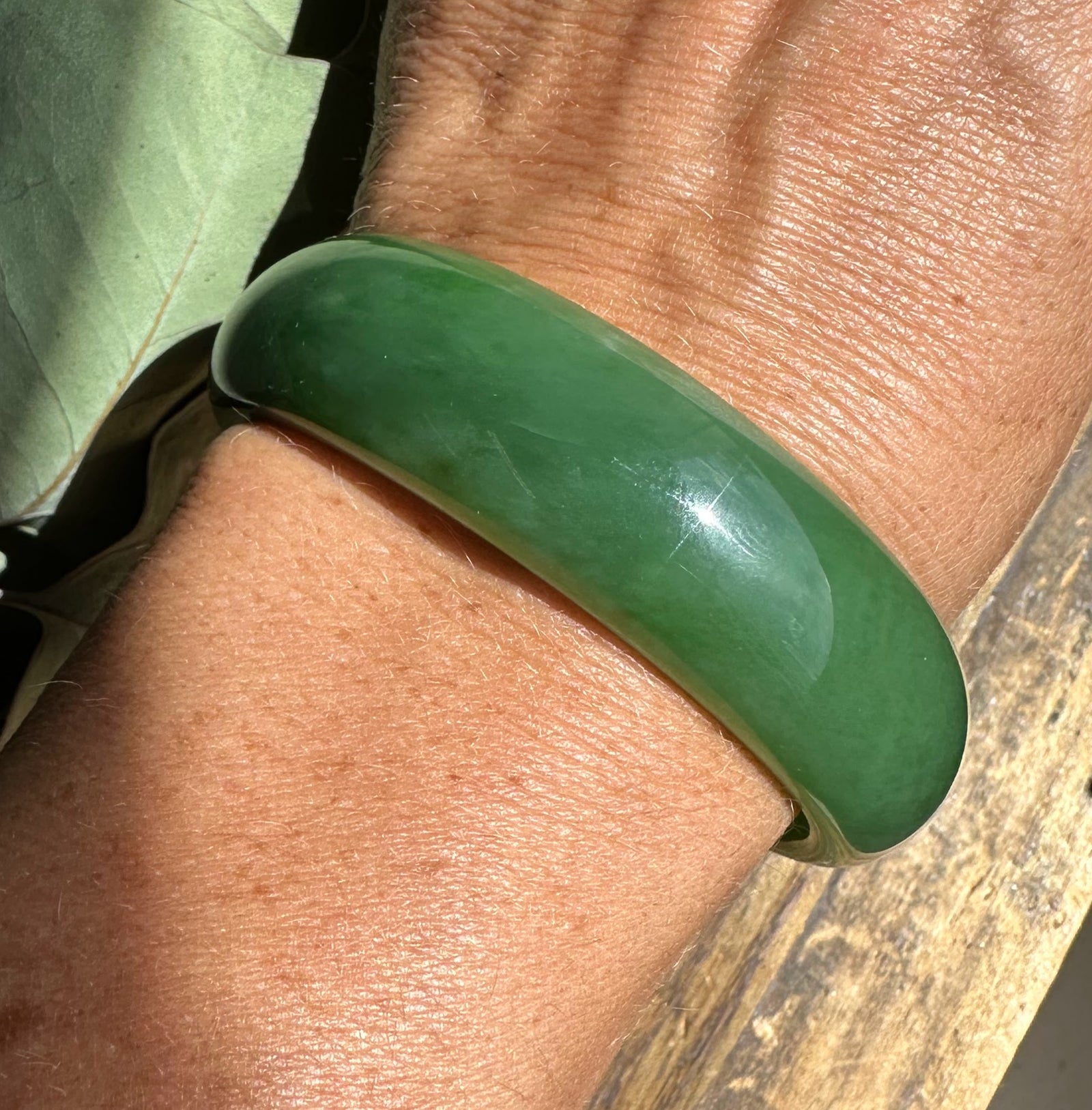 Close up of a glossy green jade bangle worn on the wrist.