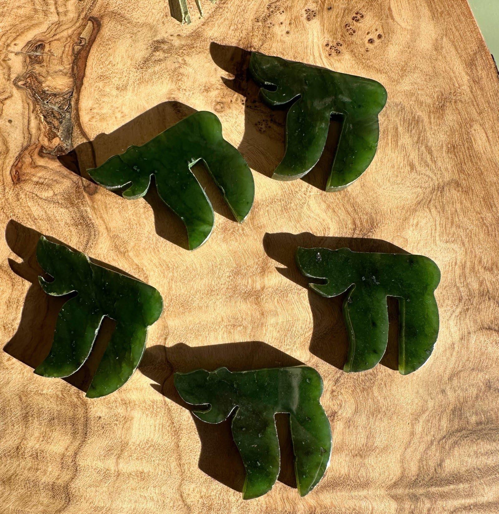 Five green jade chai pendants arranged on a wooden surface