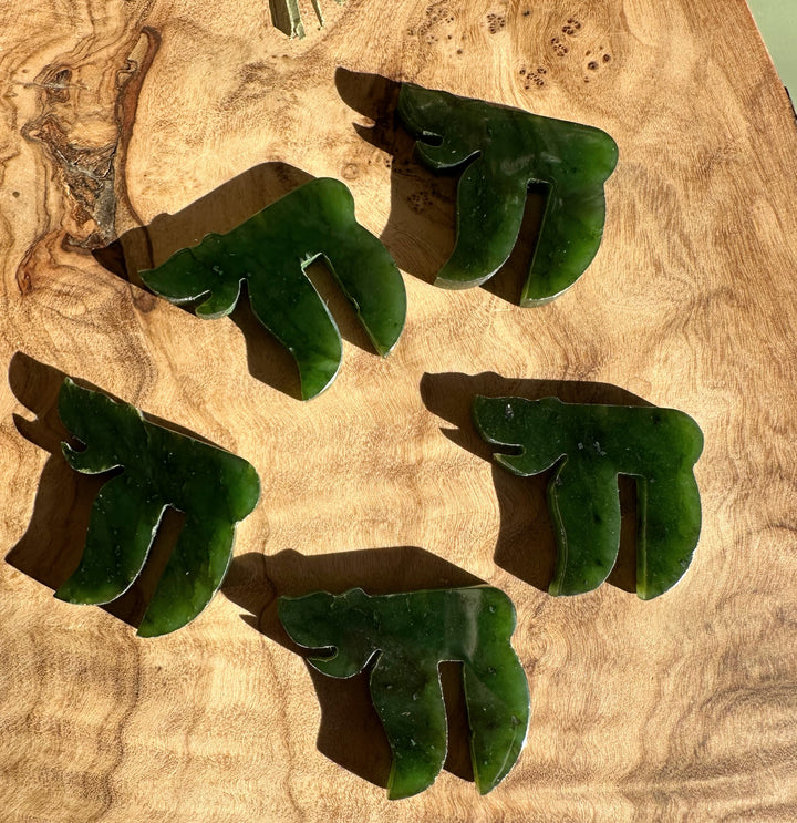 Five green jade chai pendants arranged on a wooden surface