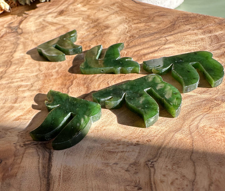 Several green jade chai pendants with gold loops arranged on a warm wood surface