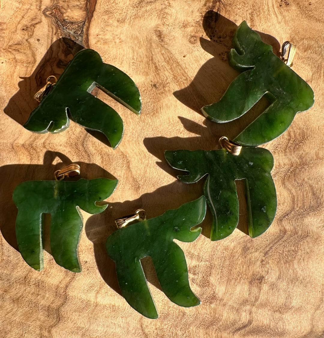 Group of vintage green jade leaf pendant charms with gold bails laid on wood