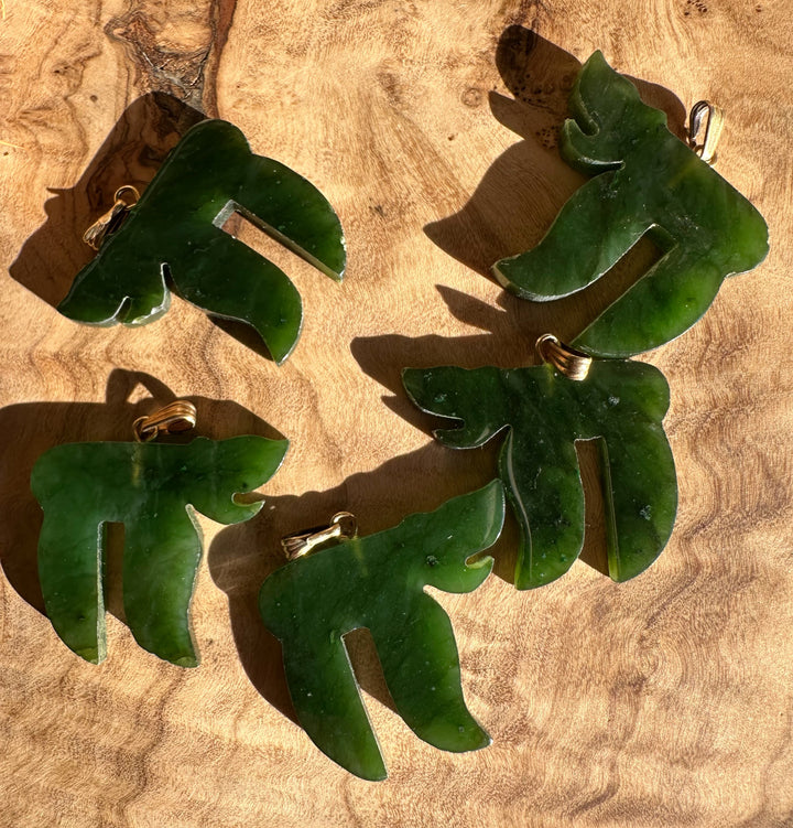 Group of vintage green jade leaf pendant charms with gold bails laid on wood