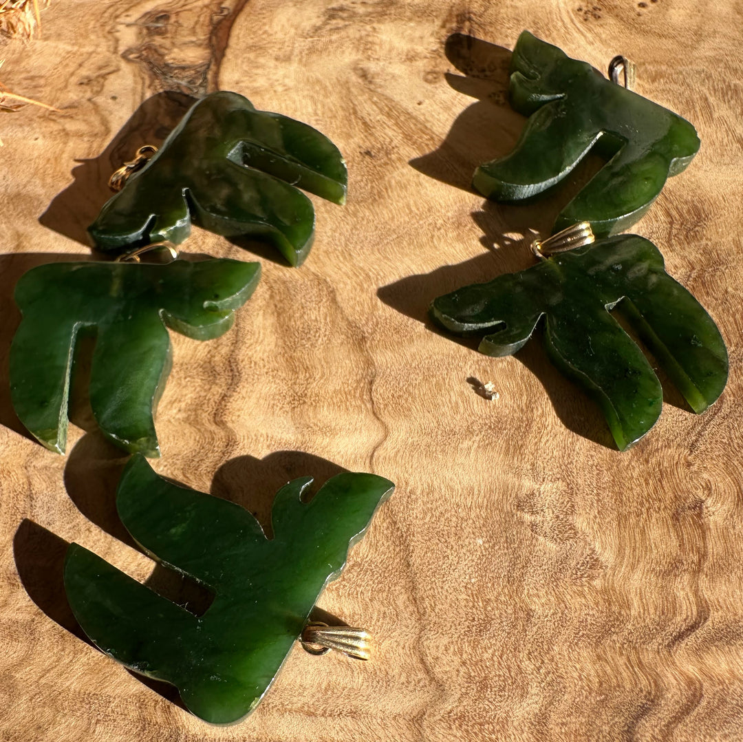 Group of vintage green jade chai pendants with gold bails on a wooden surface