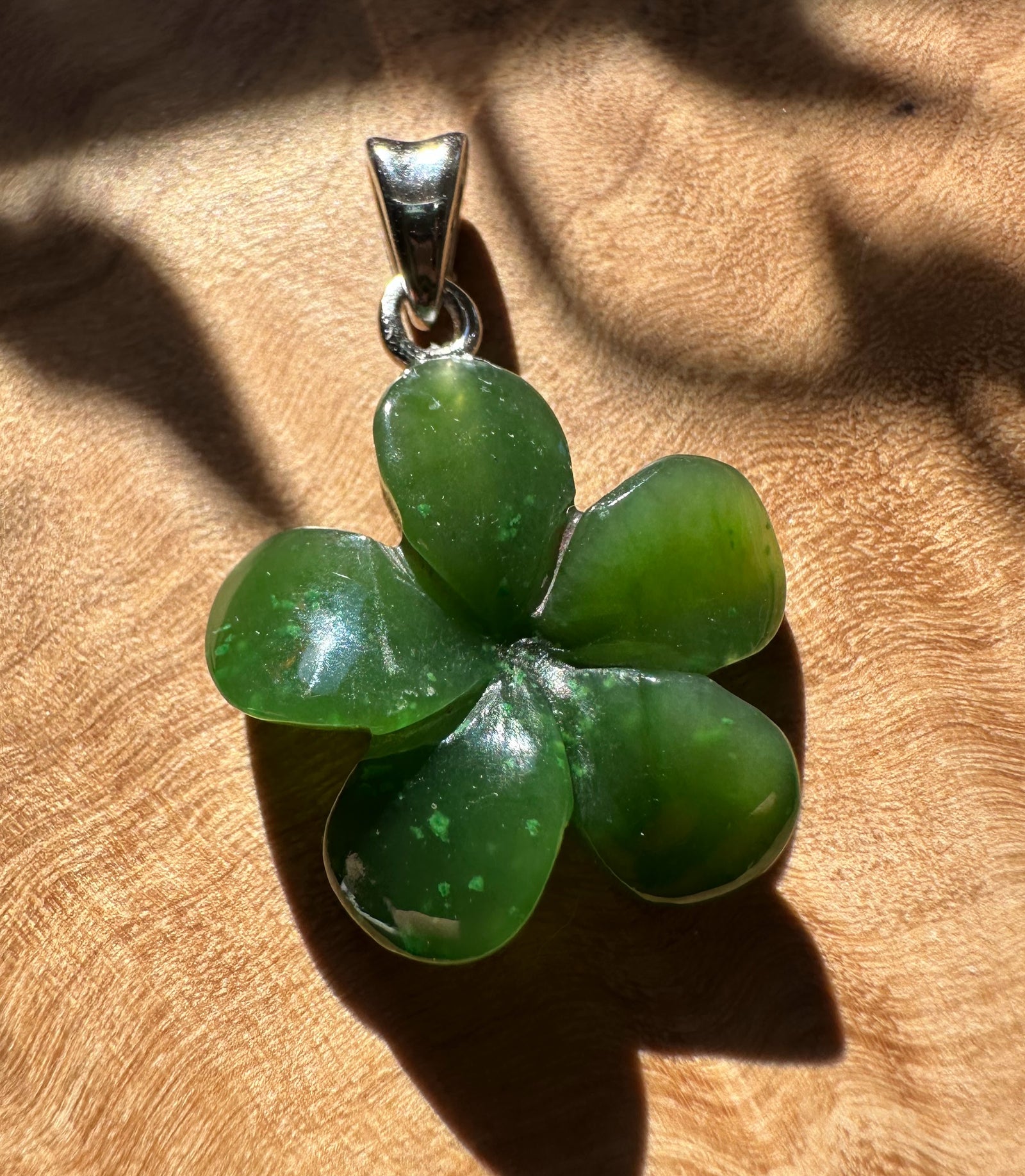 Forget Me Knot jade flower pendant with four heart-shaped petals and silver bail on brown fabric.
