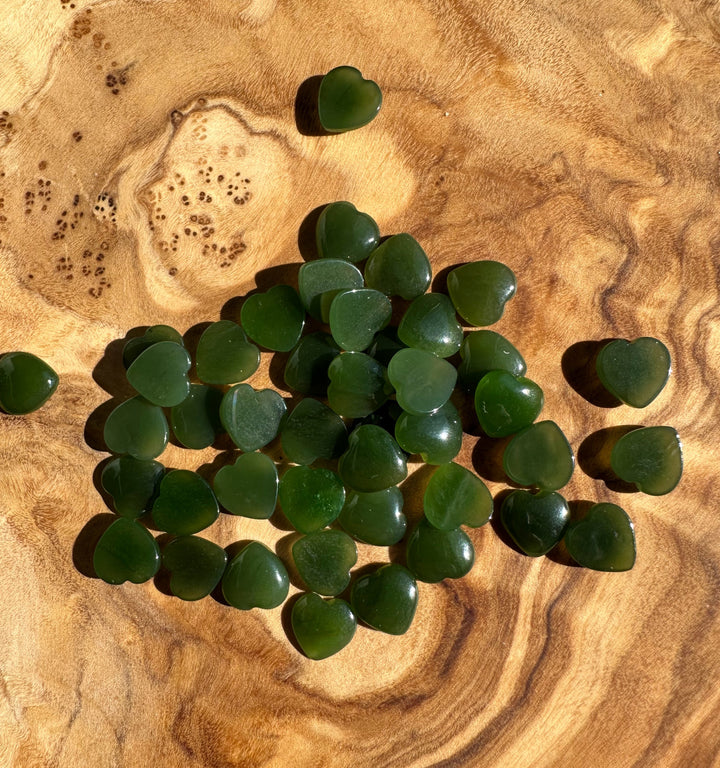 Cluster of dark green jade heart cabochons scattered on a wooden surface