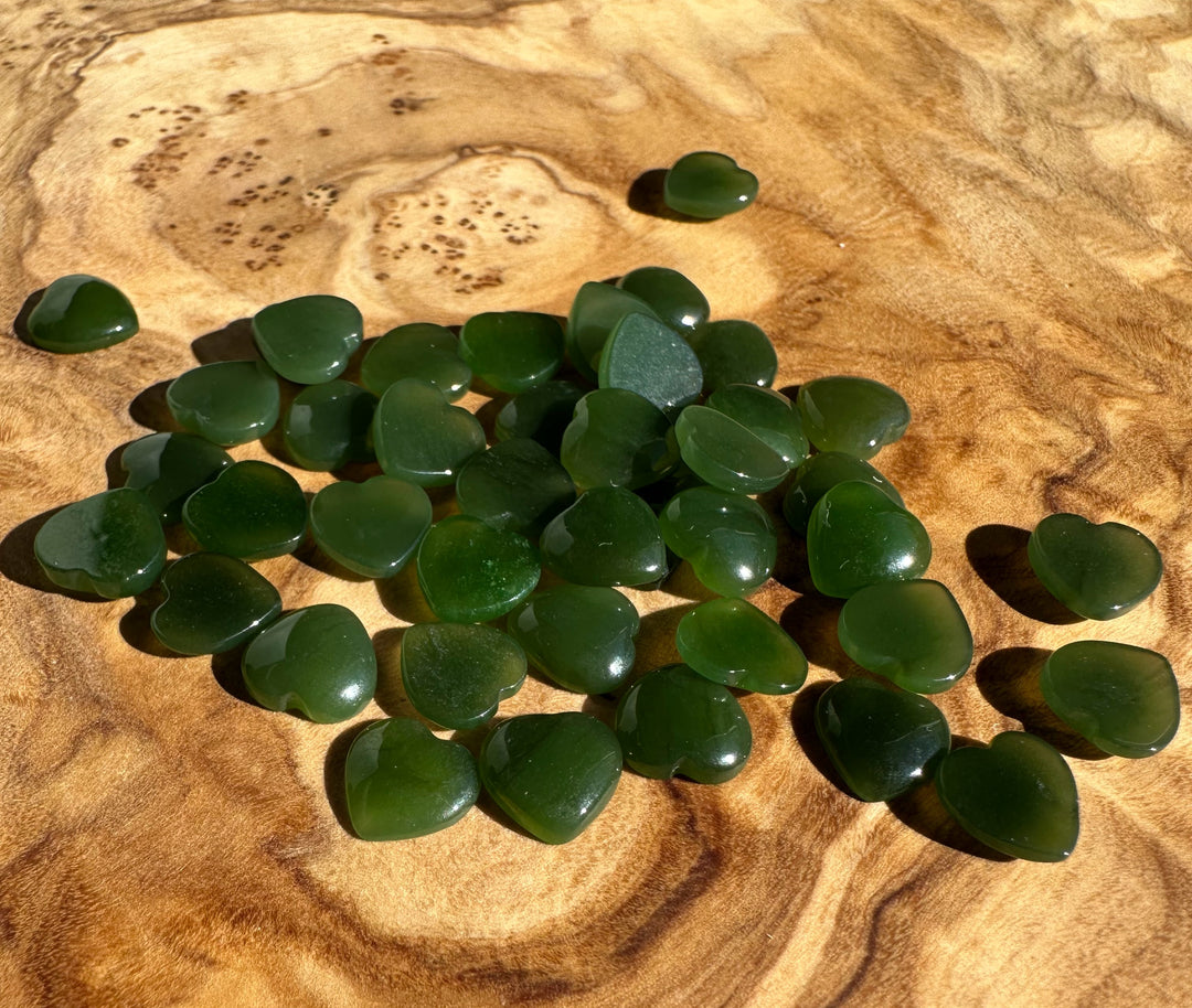 Array of dark green jade heart cabochons spread across a sunlit wooden surface