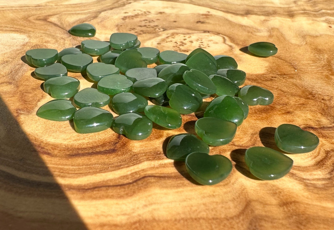 Cluster of small dark green jade heart cabochons scattered on a wood surface
