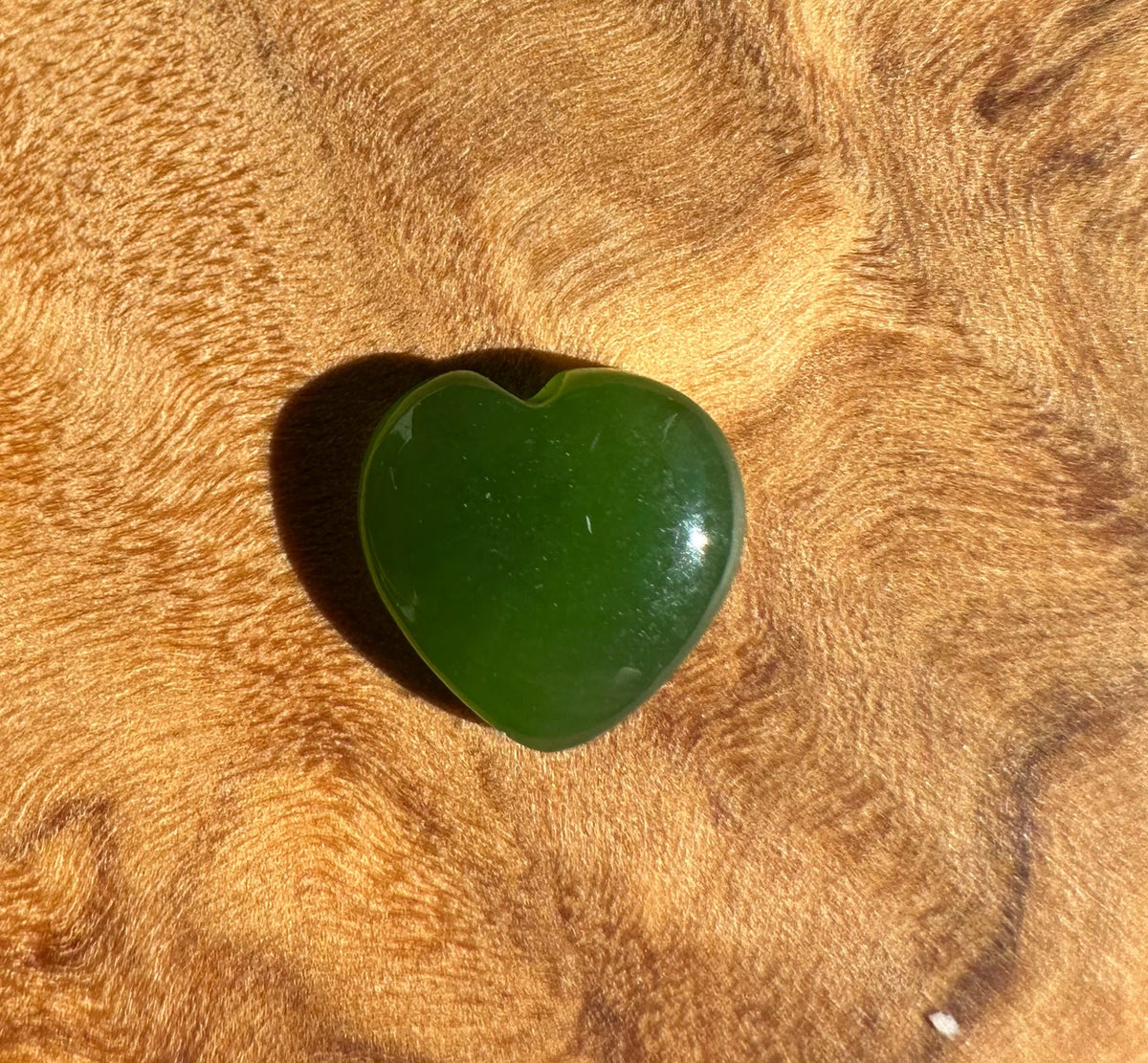 Single dark green jade heart cabochon resting on a wood background