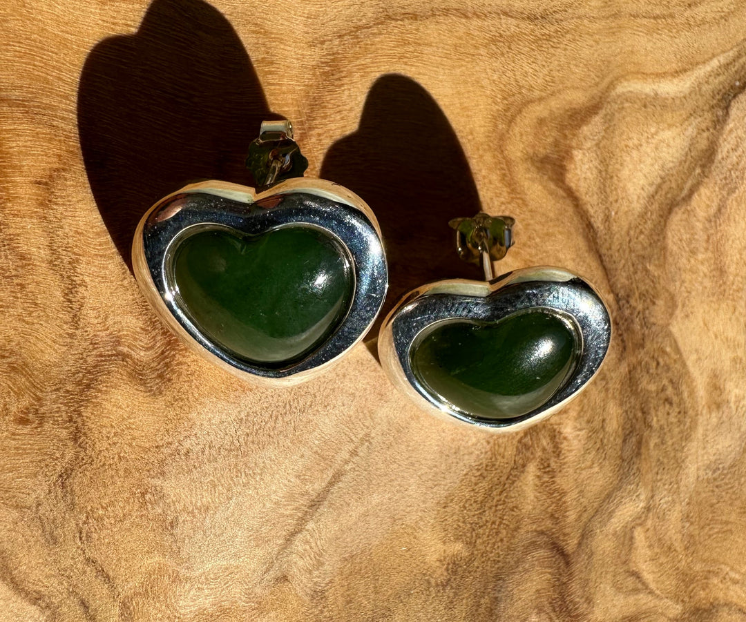 Pair of large silver heart earrings with green stone centers on a brown textured background.