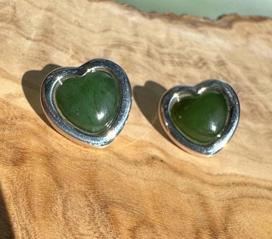 Pair of large silver heart earrings with green stones resting on a wood surface.