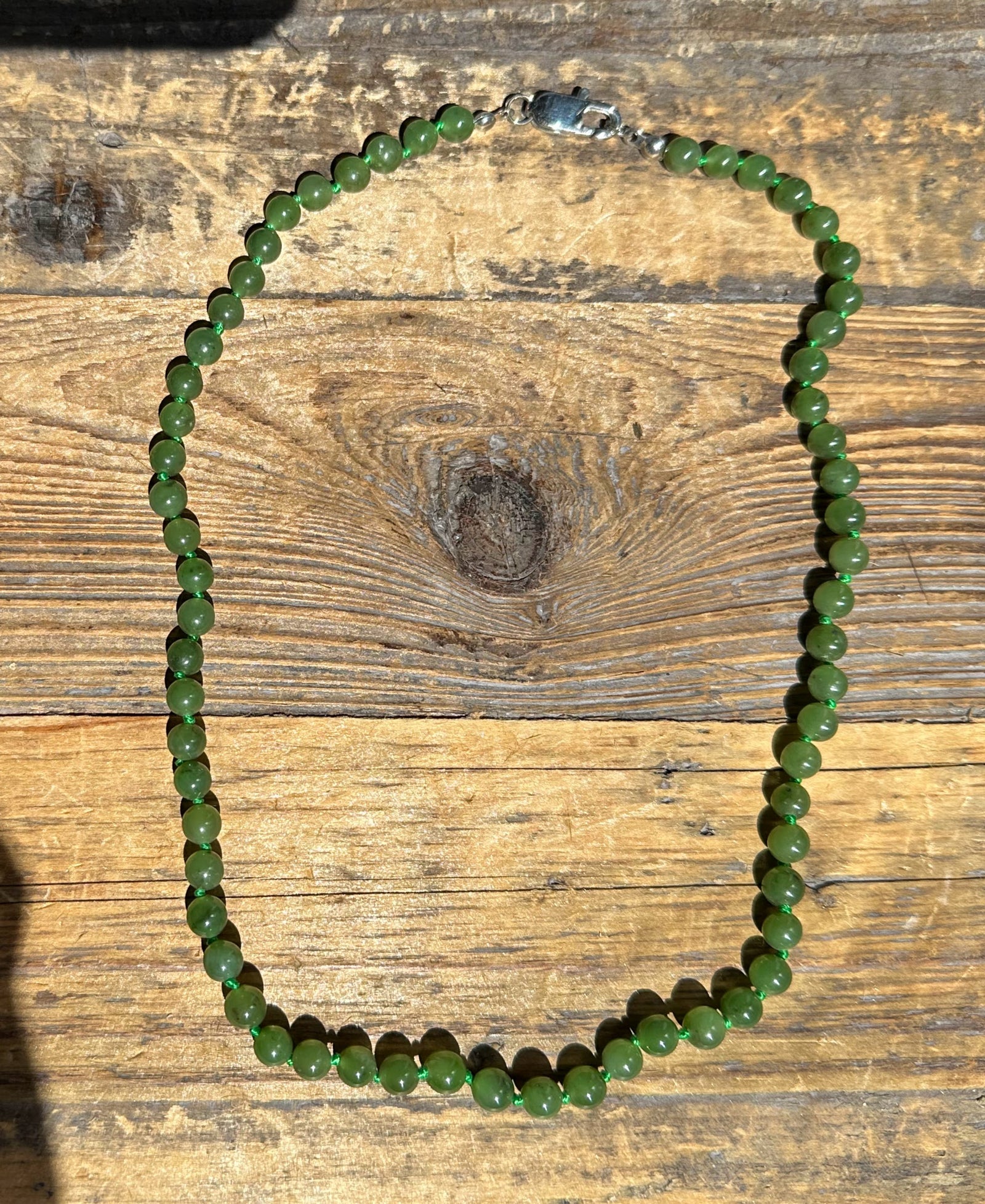 Green jade bead necklace with round beads and a metal clasp on a wooden surface.