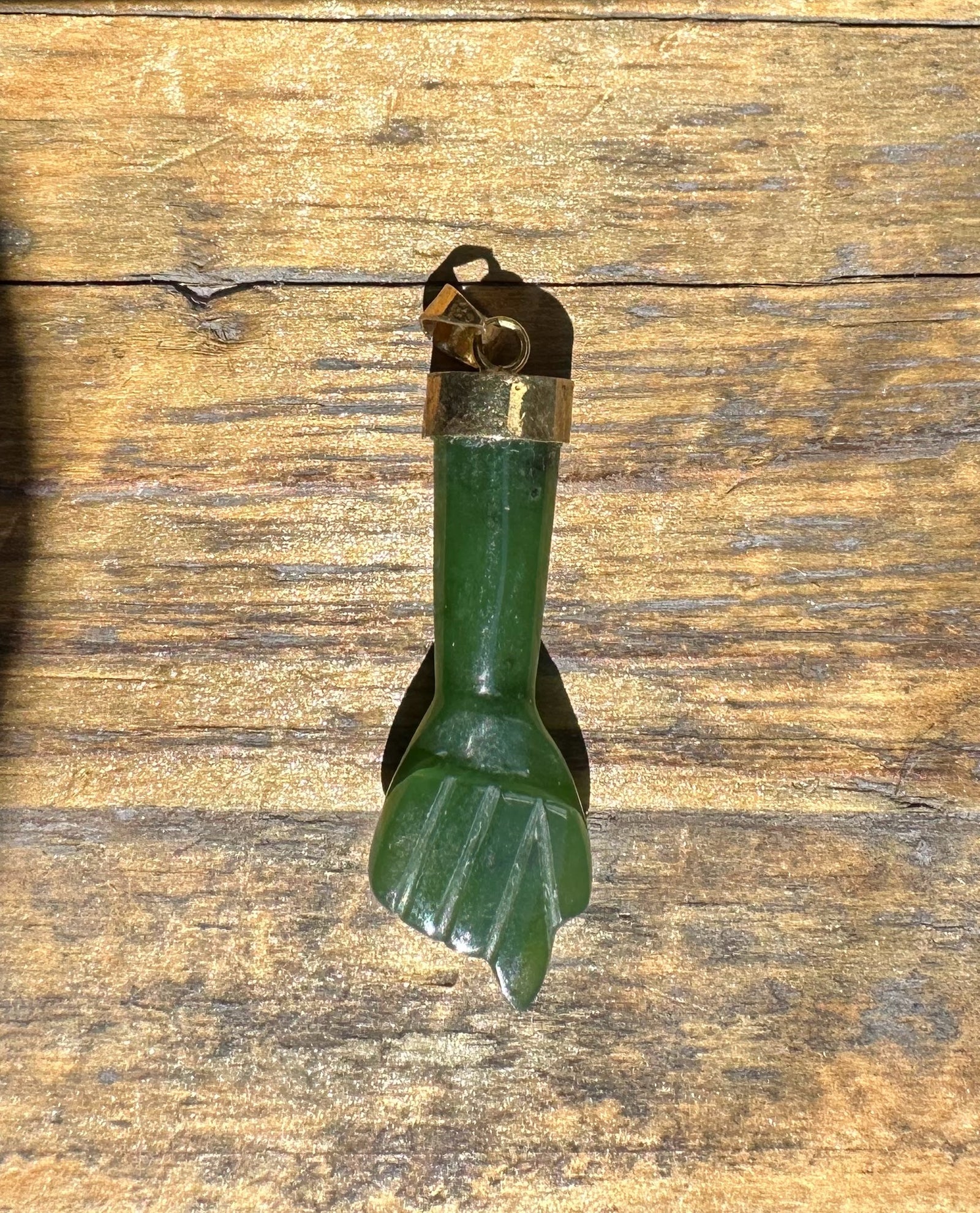 Vertical view of a vintage jade Figa pendant with brass cap and loop on a wooden surface.