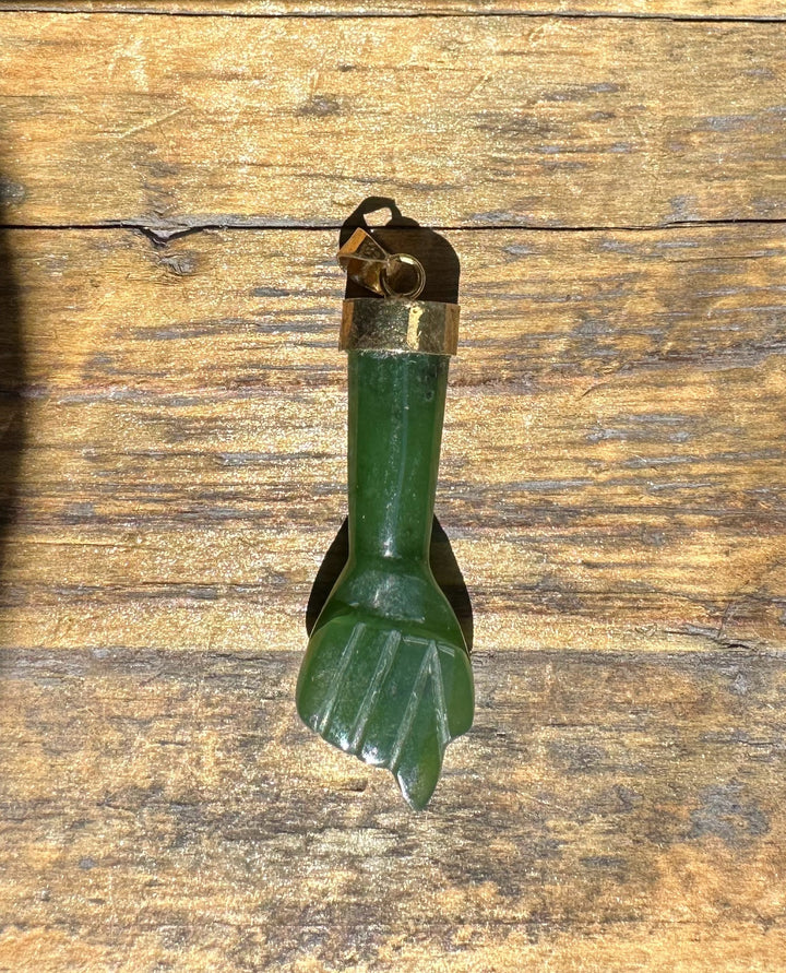 Vertical view of a vintage jade Figa pendant with brass cap and loop on a wooden surface.