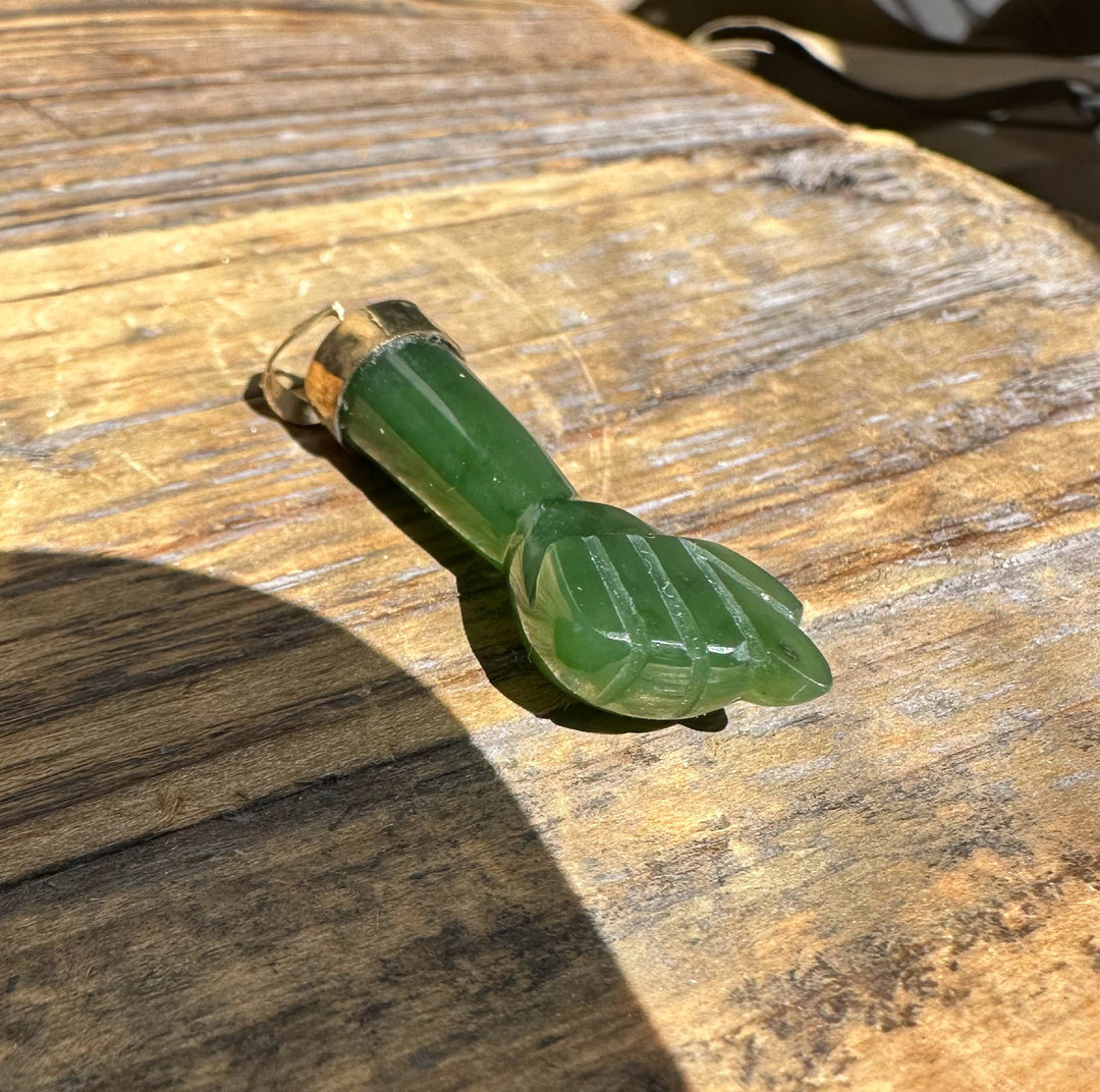 Side view of green jade Figa pendant with carved fingerlike tip resting on wood.
