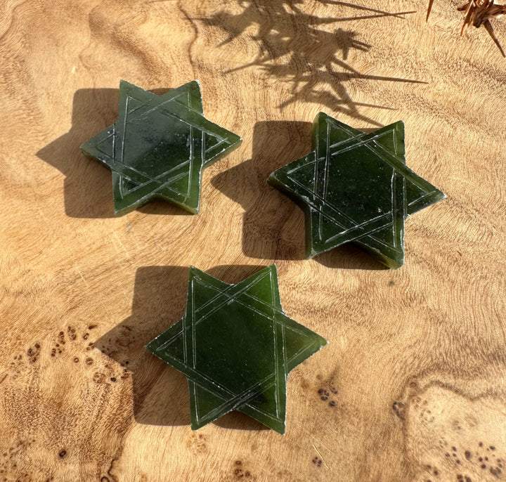 Three green jade Star of David shapes with etched lines on a wood surface